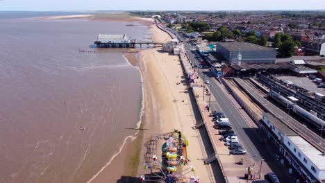 Aerial-view-above-Grimsby-Cleethorpes-seaside-fairground-along-coastline-to-holiday-pier-tourist-attraction