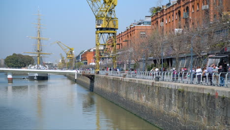 People-walking-and-staring-in-Madero-Port-with-Sarmiento-Frigate-and-yellow-crane-in-background-at-daytime-time-lapse