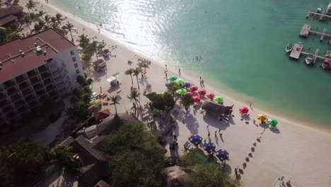 People-walking-down-Palm-Beach-in-Aruba,-next-to-people-swimming-in-the-Caribbean-Sea