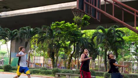 Niños-Jugando-Baloncesto-Bajo-La-Autopista-En-El-Distrito-De-Saphan-Taksin-De-Bangkok,-Tailandia,-En-Cámara-Lenta