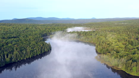 Aerial-drone-shot-above-the-mist-hanging-above-still-blue-waters-of-the-Spectacle-Ponds-in-the-green-forests-of-the-Maine-wilderness