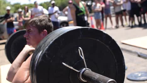 Joven-Atleta-Trabajando-Duro-Para-Completar-Un-Levantamiento-De-Sentadilla-Frontal-En-Una-Competencia-De-Crossfit