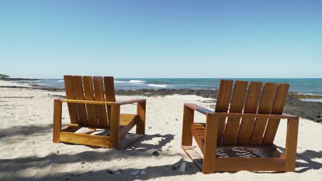 Empty-wooden-beach-chairs-facing-waves-on-a-pristine-white-sand-Hawaiian-island