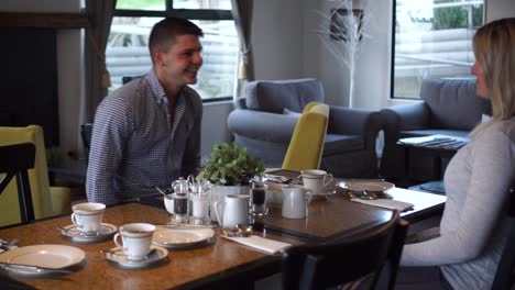 Young-attractive-couple-sitting-down-at-table-in-boutique-hotel-to-have-breakfast