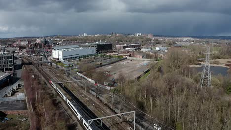 Aerial-footage-of-trains-approaching-Stoke-on-Trent-train-station-in-the-midlands-by-the-canal,-waterside-and-A50-motorway