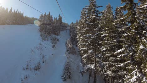 Montar-En-Un-Telesilla-Entre-árboles,-Junto-A-Una-Pista-De-Esquí-Con-Esquiadores