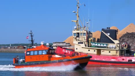 Harbour-tug-leaving-Port-of-Liepaja-in-hot-sunny-day,-orange-harbour-pilot-ship-arrives-at-port,-medium-shot