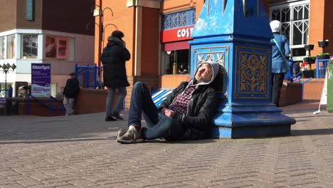 Un-Hombre-Sin-Hogar-Dormido-En-El-Centro-De-La-Ciudad-Gente-Caminando-Por-Fuera-Del-Centro-Comercial-Más-Grande-De-La-Ciudad,-Cerámicas-Intu