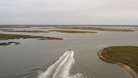 Die-Drohnenkamera-Folgt-Einem-Boot,-Während-Es-Im-Grünen-Wasser-Des-Kanals-Ein-Wunderschönes-Weißes-Kielwasser-Hinterlässt