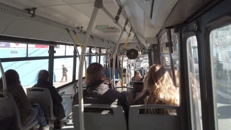 Caucasian-people-sit-on-bus-that-drives-through-crowded-street