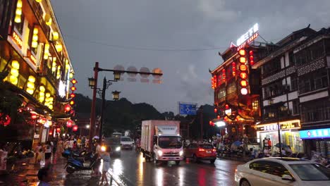 Wulingyuan,-China---August-2019-:-Bustling-life-with-cars,-traffic-and-lights-on-buildings-lit-at-night-at-a-busy-high-street-in-town-at-dusk