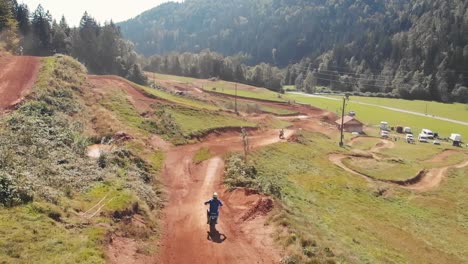 Drone-Siguiendo-A-Un-Corredor-En-Una-Moto-De-Cross-Recorriendo-Una-Pista-De-Motocross-Sobre-Los-Saltos-En-Cámara-Lenta