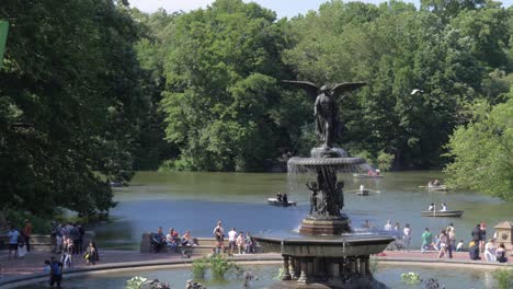 Zeitlupenaufnahme-Des-Bethesda-Brunnens-Und-Des-Dahinter-Liegenden-Sees-Mit-Menschen,-Die-Einen-Sonnigen-Sommertag-Um-Ihn-Herum-Im-Central-Park-In-New-York-City-Genießen