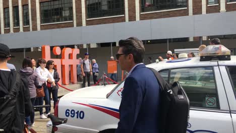 People-take-photos-of-TIFF-sign,-police-car-present,-Toronto-International-Film-Festival-2019