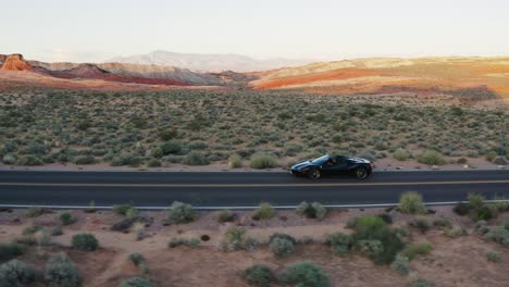 Black-Ferrari-driving-along-a-highway-in-the-Valley-of-Fire,-Nevada,-USA,-at-sunset