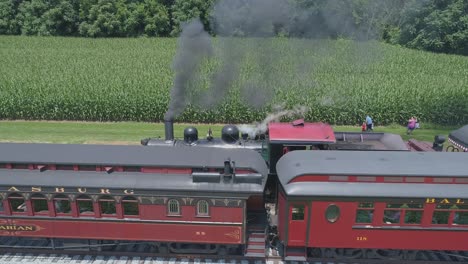 Luftaufnahme-Einer-Dampflokomotive-Aus-Dem-Jahr-1910-Mit-Einem-Rauchenden-Personenzug,-Der-Durch-Die-Amische-Landschaft-Fährt,-Während-Ein-Zweiter-Dampfzug-An-Einem-Sonnigen-Sommertag-Vorbeifährt,-Gesehen-Von-Einer-Drohne