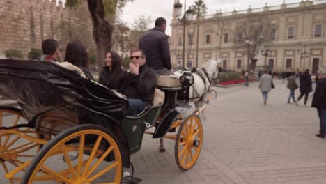 Turistas-Viajan-En-Carruaje-Tirado-Por-Caballos-En-Sevilla,-España,-Seguimiento-Pan