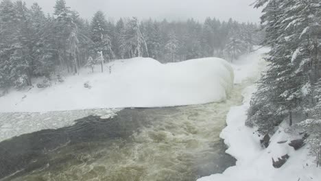 Slow-rising-drone-filming-forest's-edge-with-snow-covered-pine-trees-and-river