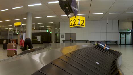 Baggage-arrival-seen-from-the-conveyor-belt-entering-an-almost-empty-International-Dutch-airport-baggage-claim-hallway-of-Schiphol-with-little-luggage