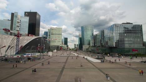 La-defense-time-lapse-with-lots-of-people-walking-fast-and-clouds-reflecting-in-the-tall-modern-buildings-in-Paris,-wide-still-timelapse-during-cloudy-day