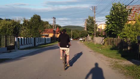 Moreni,-Romania---13-July-2020-:-Guy-wearing-black-riding-bike-on-a-country-road-at-sunset,-slow-motion