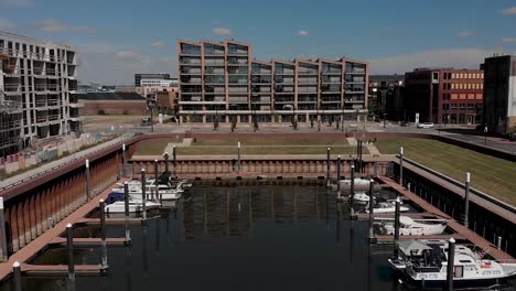 Backward-aerial-movement-showing-small-Dutch-recreational-port-Noorderhaven-with-pleasure-boats-laying-anchor,-contemporary-apartment-building-in-the-background