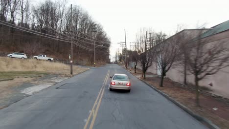 Close-up-drone-following-tracking-shot-of-car-going-up-hillside-road-during-winter-in-Reading-Pennsylvania