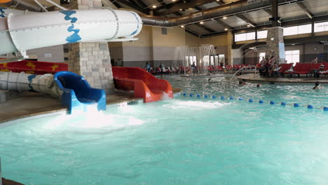 Imágenes-Panorámicas-De-Una-Piscina-Cubierta,-Una-Fuente-Y-Niños-Jugando,-Con-Dos-Toboganes