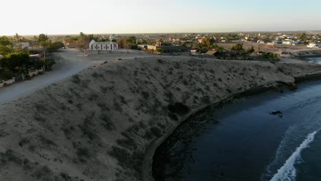 Aerial-view-Moving-forward-shot,-Shoreline-on-the-low-tide-in-San-Juanico,-California-Sur,-Mexico,-Scenic-view-of-town,-White-church-in-the-background