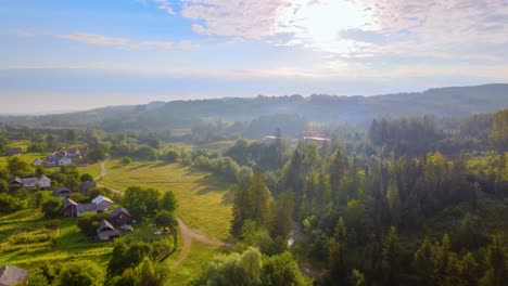 Aerial-view-over-road,-houses-and-lush-green-nature,-in-the-Carpathian-Mountains,-misty,-summer-day,-in-Ukraine---tilt-up,-drone-shot