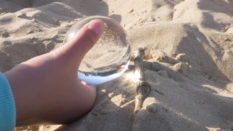 Hobby-crystal-ball-magnify-burning-wood-on-beach-closeup
