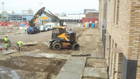 Deliberation-among-construction-workers-and-operating-of-heavy-machinery-placing-large-paving-stones-of-a-provisional-sidewalk-in-front-of-newly-build-houses-in-the-rain