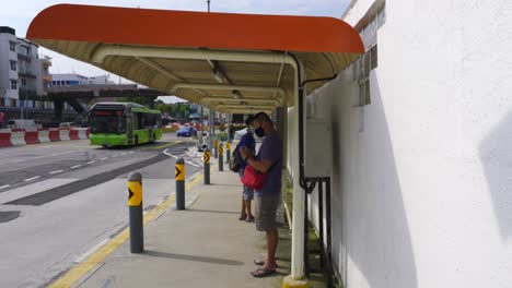 Hombre-Chino-Con-Mascarilla-Y-Usando-Teléfono-Móvil-Mientras-Espera-El-Autobús-En-Singapur,-Asia