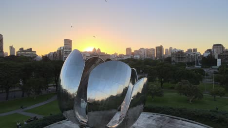 Foque-Volando-Sobre-La-Escultura-De-Acero-Floralis-Generica-Al-Atardecer-Con-Rayos-De-Sol-Detrás-De-Los-Edificios-De-La-Recoleta