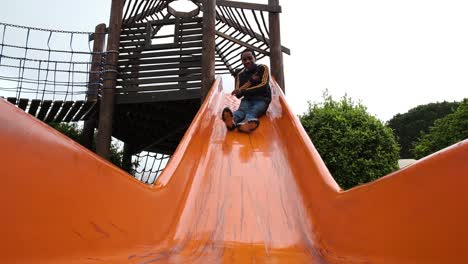 Happy-smiling-black-male-youth-sliding-and-playing-on-colourful-play-area-slide