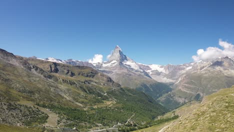 Slow-drone-shot-moving-backwards-showing-the-vast,-massive-and-lush-valley-in-Zermatt,-Switzerland-with-mountain-Matterhorn-in-the-background