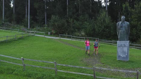 Female-Hikers-Walk-Towards-Bronze-Statue-Of-Lovro-Kuhar-In-Kotlje