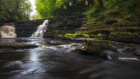 Panorama-Zeitraffer-Des-Wasserfalls-Im-Frühlingswald,-Umgeben-Von-Bäumen-Mit-Felsen-Im-Vordergrund-In-Der-Ländlichen-Landschaft-Irlands