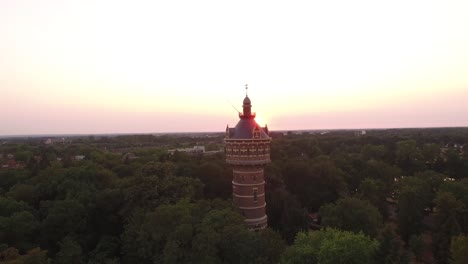 Una-órbita-De-ángulo-Bajo-Alrededor-De-Una-Torre-De-Agua-Con-Una-Brillante-Puesta-De-Sol-En-El-Fondo