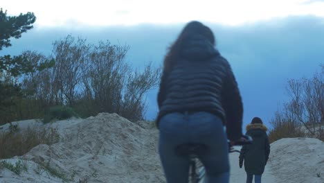 Brunette-girl-and-two-people-with-bikes-crossing-seaside-dunes