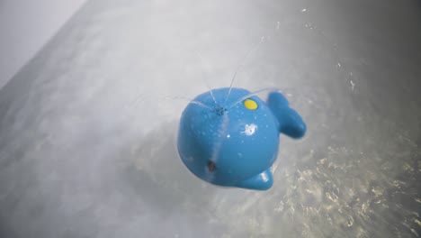 Ein-Blauer-Wasserspielzeugwal,-Der-Sich-In-Einer-Badewanne-Dreht-Und-Wasser-Herumspritzt