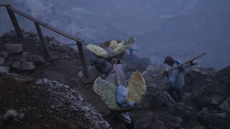 Kawah-Ijen-Schwefelbergbauarbeiter-Wandern-Durch-Felsiges-Gelände-Und-Tragen-Schwere-Lasten-Im-Frühen-Morgenlicht