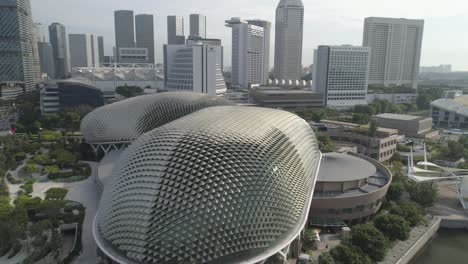 Nahflug-Um-Das-Berühmte-Esplanade-Theater-In-Singapur-An-Der-Marina-Bay-Mit-Den-Wolkenkratzern-Der-Skyline-Der-Stadt-Im-Hintergrund-Und-Dem-Vorbeiziehenden-Autoverkehr