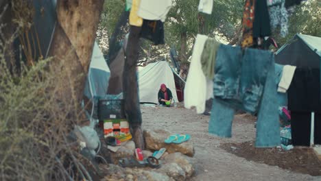 Eine-ältere-Frau-Wäscht-In-Einem-Flüchtlingslager-Geschirr,-Im-Vordergrund-Hängt-Kleidung-An-Einer-Leine