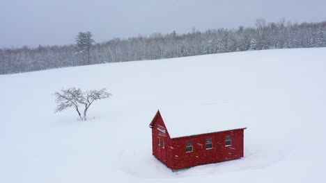 Flying-past-a-red-barn-and-an-apple-tree-on-a-snow-covered-hill-side-field-AERIAL-SLOW-MOTION