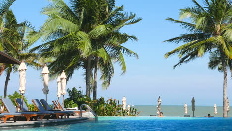 Thailand---Circa-Infinity-Pool-Am-Pool-Und-Meerblick-In-Einem-Luxuriösen-Tropischen-Hotel-An-Einem-Windigen-Sommertag-Mit-Weißen-Sonnenschirmen,-Strandliegen-Und-Palmen