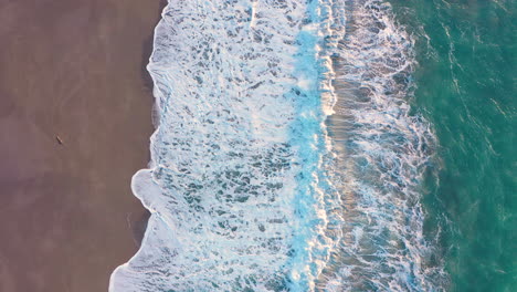 Drone-slowly-descending-over-turquoise-ocean-and-beach-and-waves-coming-ashore