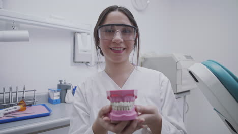 Lächelnde-Zahnärztin,-Die-Mit-Einem-Zahnmodell-An-Ihren-Händen-Die-Grundstruktur-Des-Mundes-Zeigt