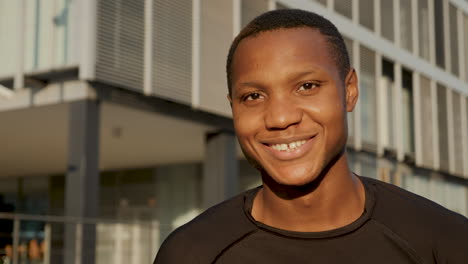 Portrait-of-young-black-man-smiling-and-looking-at-camera-outdoors.-Handsome-african-american-male-athlete-resting-on-a-sunny-afternoon.-Close-up.