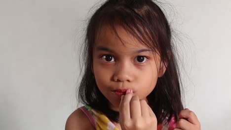 Slowmo-shot-of-a-cute-asian-toddler,-with-big-round-eyes,-seriously-applying-lipstick-by-herself
